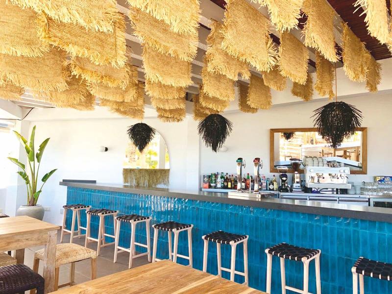 Moderner Hotelbarbereich mit blauer Theke, Holzstühlen und dekorativem Deckenhimmel aus Stoffbahnen.