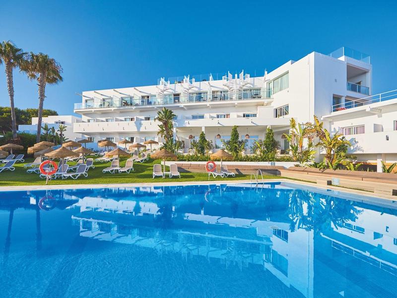 Moderner Hotelkomplex mit Swimmingpool und Liegestühlen unter klarem blauem Himmel.