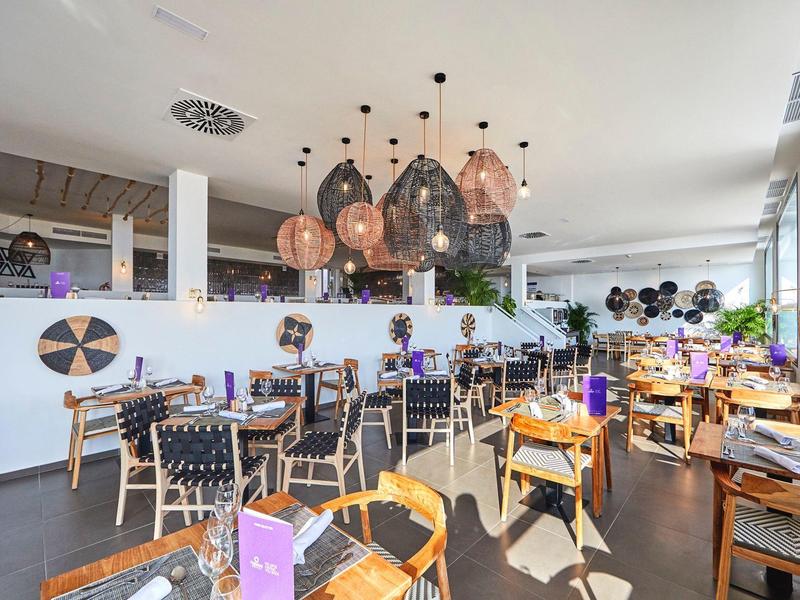 Modernes Restaurant mit Holztischen, zugewandten Stühlen und dekorativen Hängelampen in hellem Raum