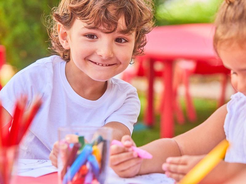 Zwei Kinder sitzen draußen an einem Tisch und malen mit bunten Stiften.