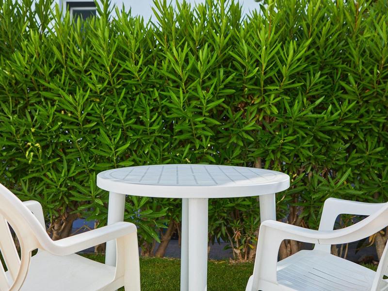 Weißer runder Tisch mit zwei weißen Plastikstühlen vor grünem Busch