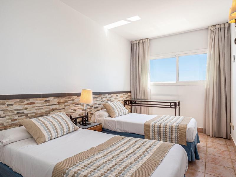 Helles Hotelzimmer mit zwei Einzelbetten und Fenster mit Meerblick.