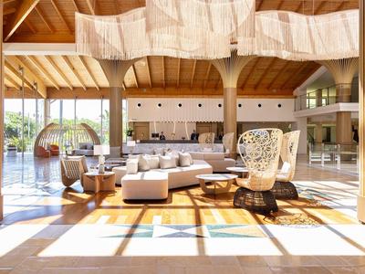 Geräumiger Hotel-Loungebereich mit modernen Möbeln, großen Fenstern und Holzdecken.