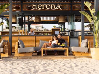 Paar entspannt sich auf einem Sofa am Strand neben einer Bar namens Serena.