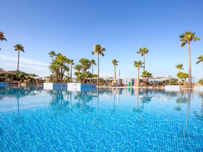 Großer blauer Pool mit Palmen und blauem Himmel im Hintergrund an einem sonnigen Tag.