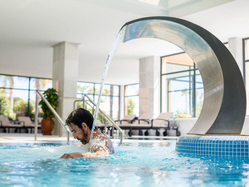 Innenpool mit einer großen Wasserfontäne und einer Person, die im Wasser schwimmt.