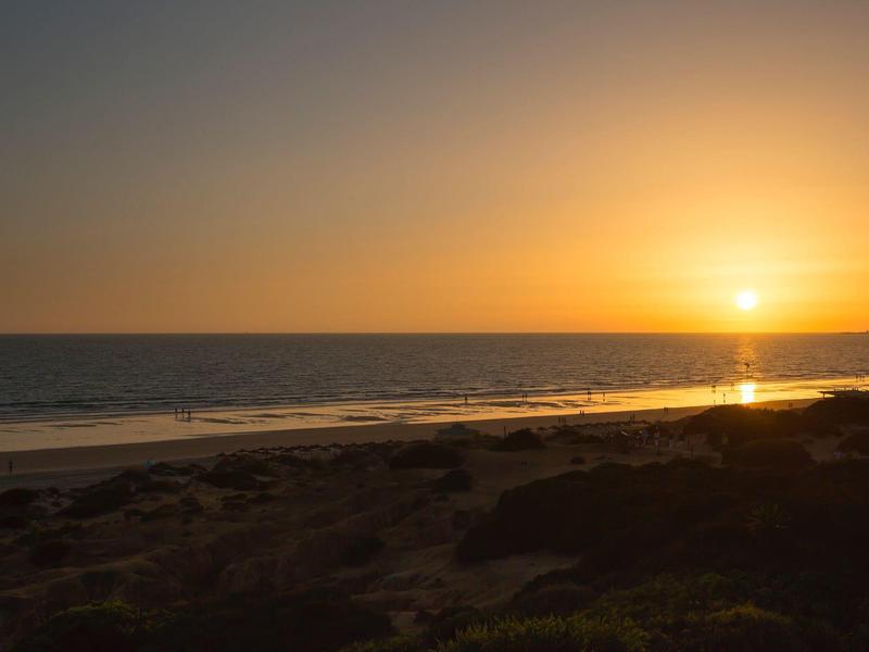 Sonnenuntergang am Meer mit orangefarbenem Himmel und dunklem Strand im Vordergrund.