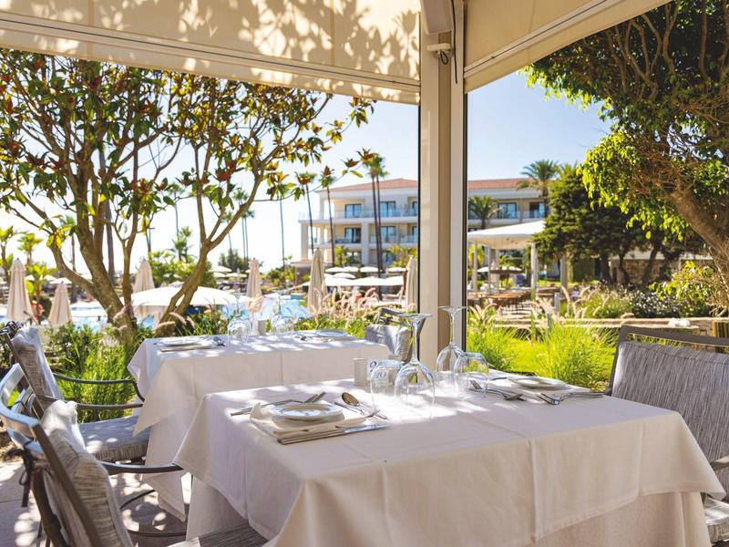 Terrassenrestaurant mit gedecktem Tisch, weißen Decken, Stühlen und grüner Bepflanzung.
