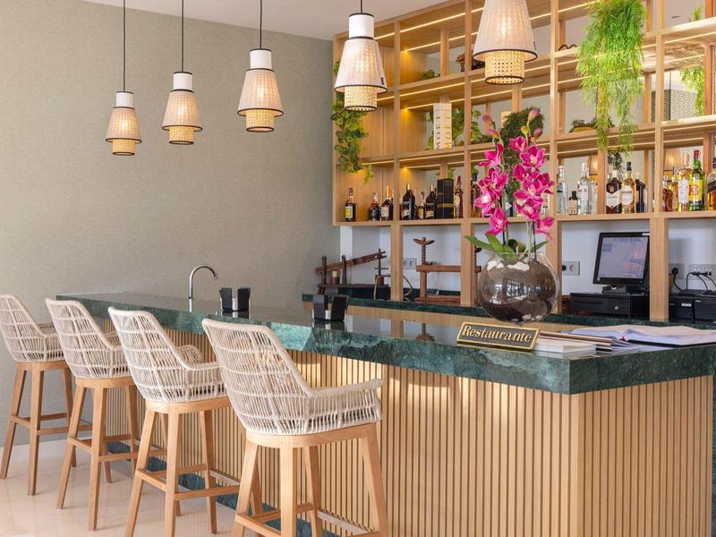 Moderner Barbereich mit hölzernen Stühlen, grüner Marmorplatte und hängenden Lampen.