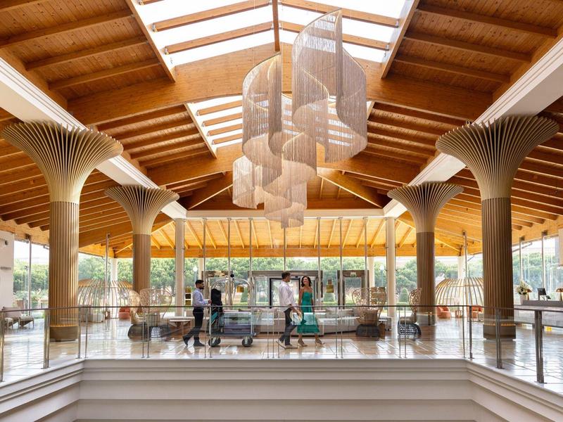 Innenraum eines Einkaufszentrums mit Holzdecken, großen Säulen und hängenden Lampenschirmen.