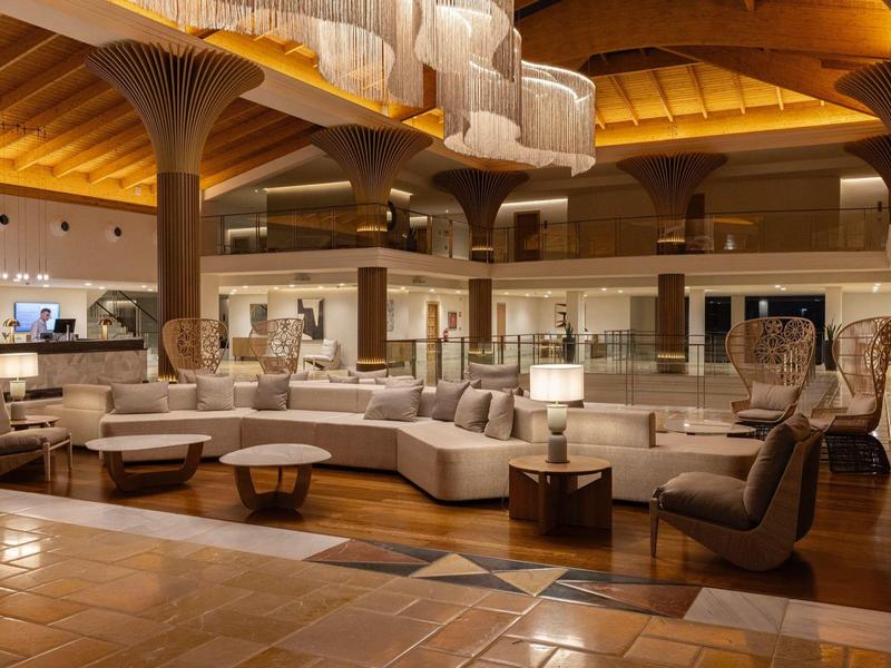 Großer, moderner Loungebereich mit geschwungenen Sofas, Holzsäulen und warmem Deckenlicht.