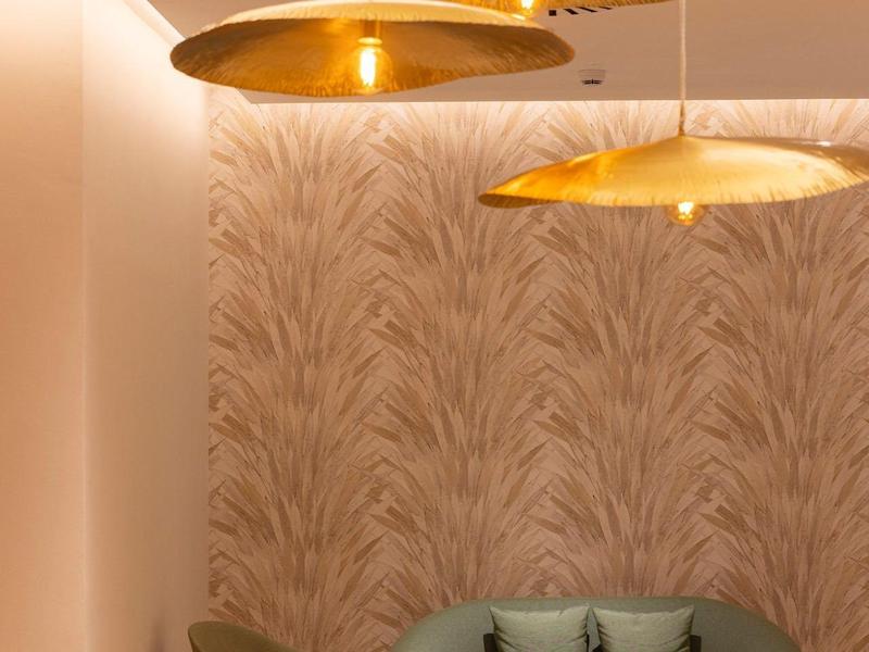 Gemütliche Ecke mit grünem Sofa, kleinem Tisch, Stuhl und goldenen Hängelampen an Teppichwand.