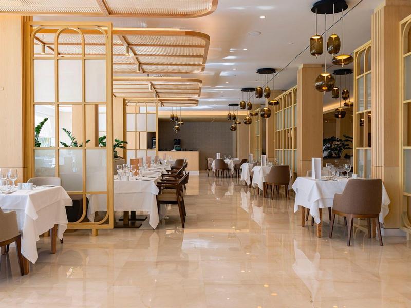 Elegantes Restaurant mit hellem Marmorboden, weißen Tischdecken und goldfarbenen Raumteilern.