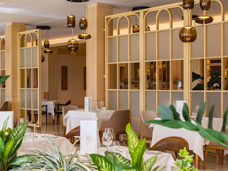 Moderner Speiseraum mit weißen Tischen, goldfarbenen Trennwänden und grünen Pflanzen.