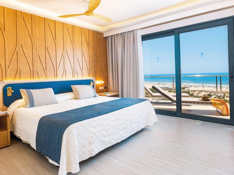 Helles Schlafzimmer mit großem Bett, blauen Akzenten und Meerblick durch eine Glas-Schiebetür.