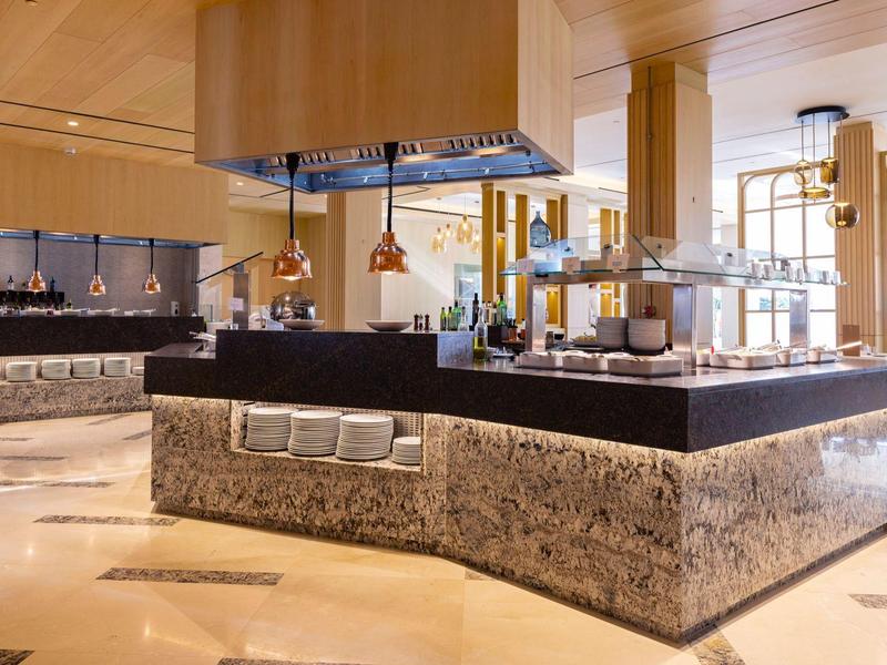 Elegante Buffetinsel mit Granitbasis, schwarzen Abdeckungen und Kupfer-Deko in hellem Raum.