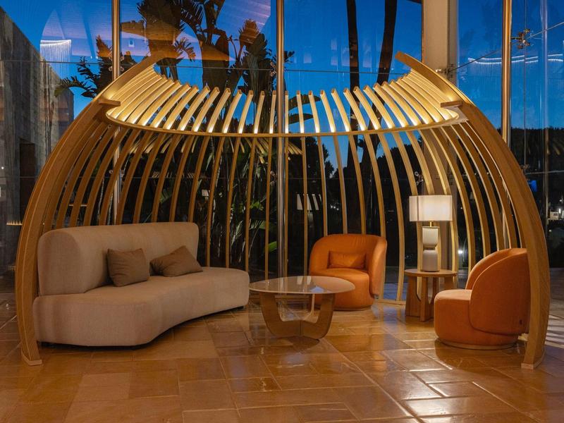 Moderne Lounge mit geschwungener Holzstruktur, bequemen Sesseln und weicher Beleuchtung am Abend.