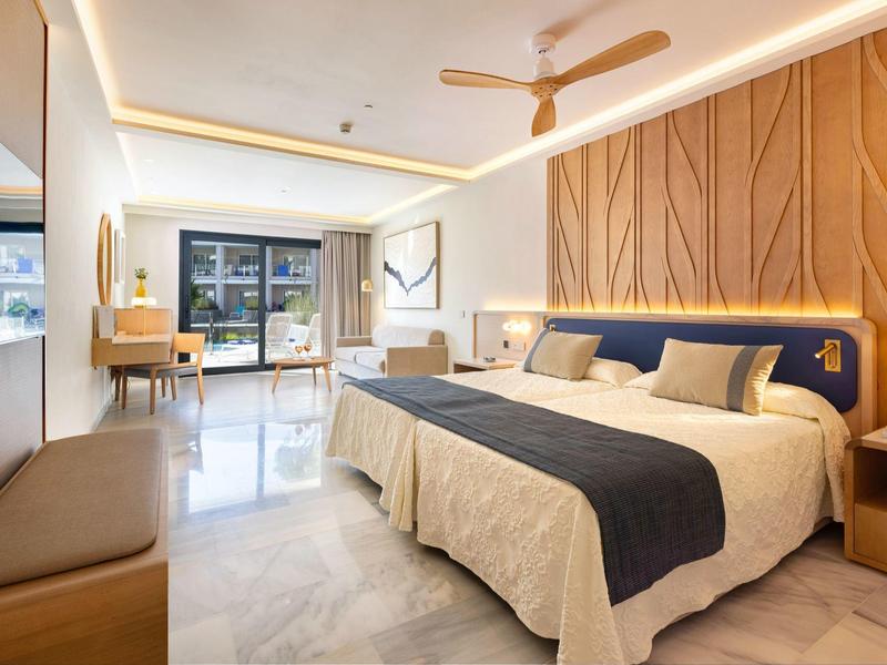 Helles Hotelzimmer mit großem Doppelbett, Holzakzenten und modernem, minimalistischem Design.