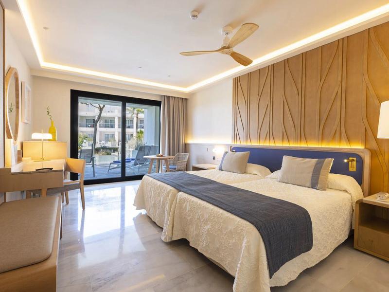 Modernes Hotelzimmer mit großen Betten, hellen Wänden, Holzakzenten und Terrasse mit Poolblick.