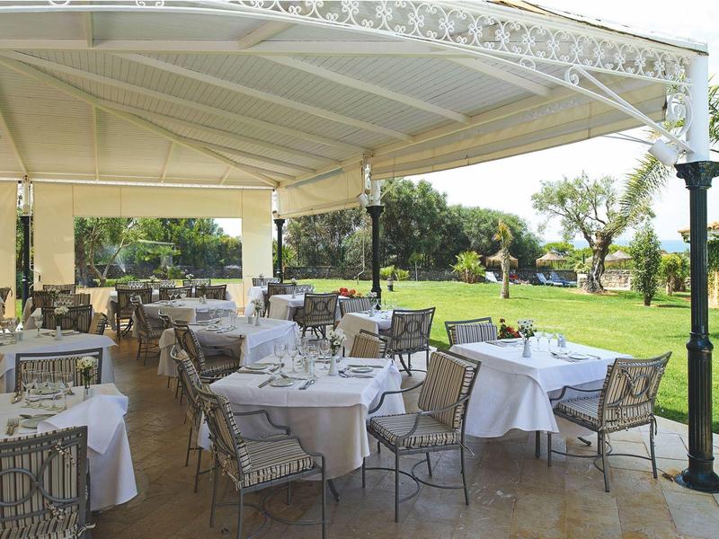 Überdachte Terrasse mit gedeckten Tischen und Stühlen, umgeben von grüner Wiese und Bäumen.