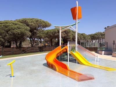 Flaches Planschbecken mit bunten Rutschen und Wasserfontänen unter blauem Himmel.