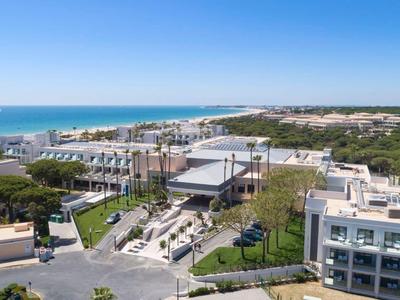 Moderne Hotelanlage an der Küste mit Blick auf Meer und bewaldete Landschaft.