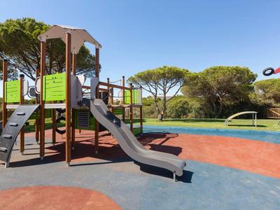 Spielplatz mit Klettergerüst und Rutsche neben einem Pool im Freien unter blauem Himmel