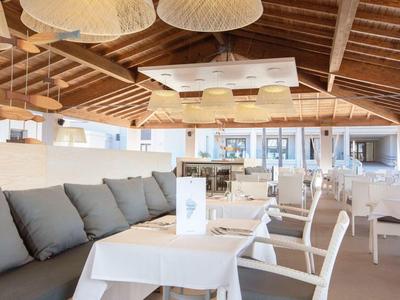 Helles Restaurant mit Holzdach, weißen Tischen und gepolsterten Sitzbänken und Stühlen.