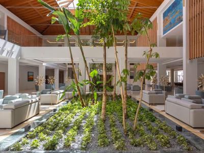 Helles Hotelinterieur mit Pflanzenbeet und gemütlichen Sitzbereichen unter Holzdecke.
