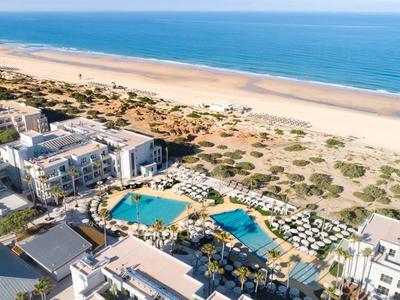 Luftaufnahme eines Hotelkomplexes mit mehreren Pools neben einem langen Sandstrand.