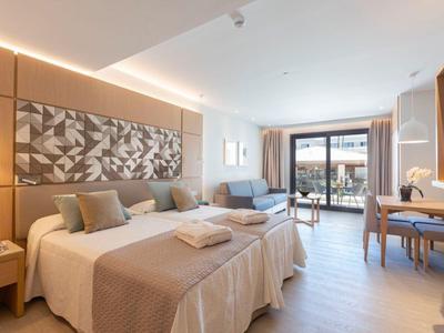 Helles Hotelzimmer mit zwei Betten, Sofa, Schreibtisch und Balkon mit Blick nach draußen.