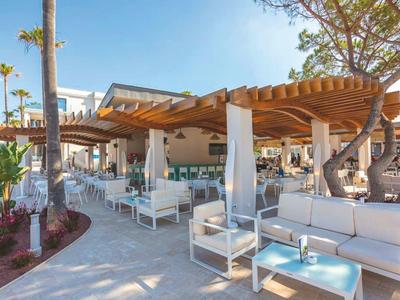 Moderner Außenbereich mit weißen Loungemöbeln und Holzpergola in Hotelanlage bei klarem Himmel.