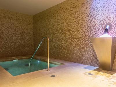 Luxuriöser Whirlpool in einem eleganten, mit goldfarbenen Mosaikfliesen bedeckten Raum.