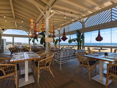 Offenes Restaurant mit Holzboden, Korbstühlen und Meerblick unter einem überdachten Dach.