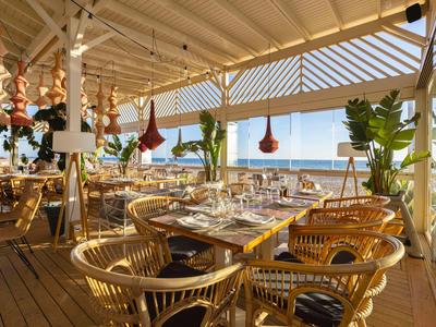 Offenes Restaurant mit Weitblick aufs Meer, Holzdecke und modernen Korbstühlen.