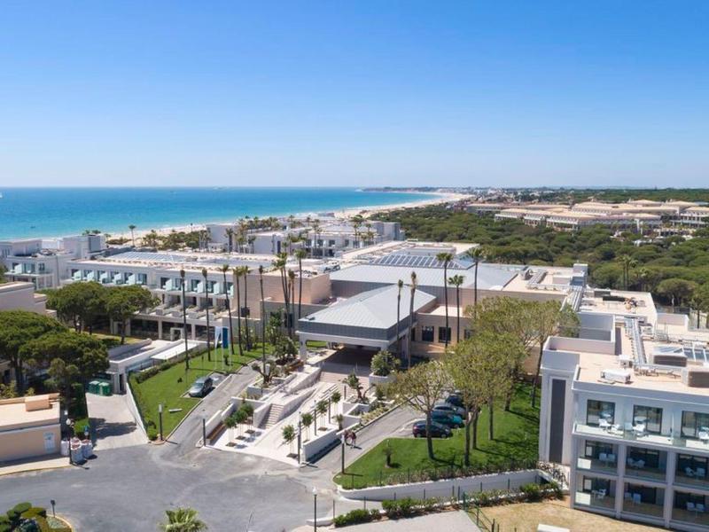 Moderne Hotelanlage an der Küste mit Blick auf Meer und bewaldete Landschaft.