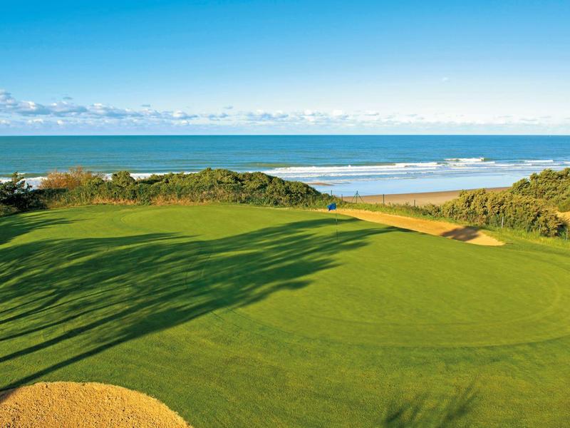 Grüner Golfplatz mit Sandbunkern an einem Küstenabschnitt unter blauem Himmel
