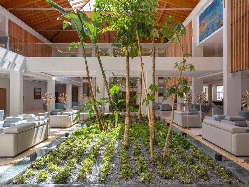 Helles Hotelinterieur mit Pflanzenbeet und gemütlichen Sitzbereichen unter Holzdecke.