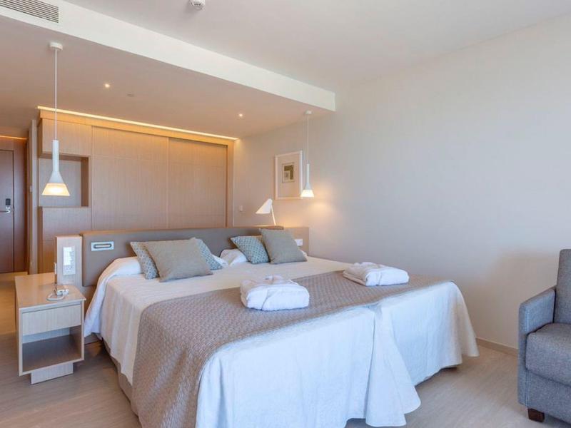 Modernes Hotelzimmer mit zwei Einzelbetten, Nachttisch, Leselampen und einem grauen Sessel.