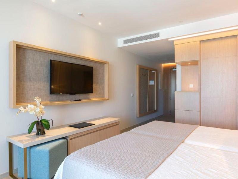 Schlicht eingerichtetes Hotelzimmer mit zwei Einzelbetten, TV und Nachttisch mit Blume.