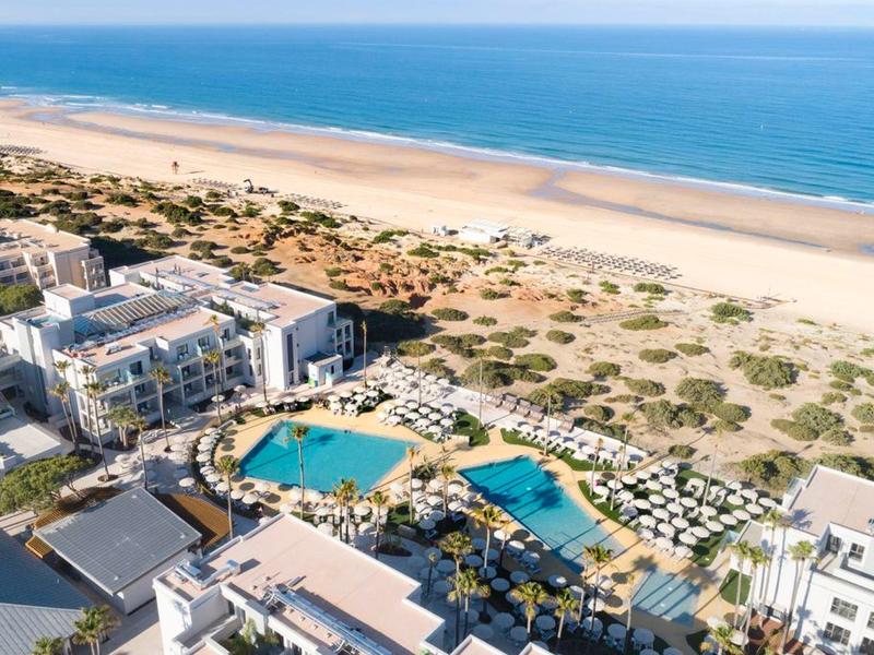 Luftaufnahme eines Hotelkomplexes mit mehreren Pools neben einem langen Sandstrand.