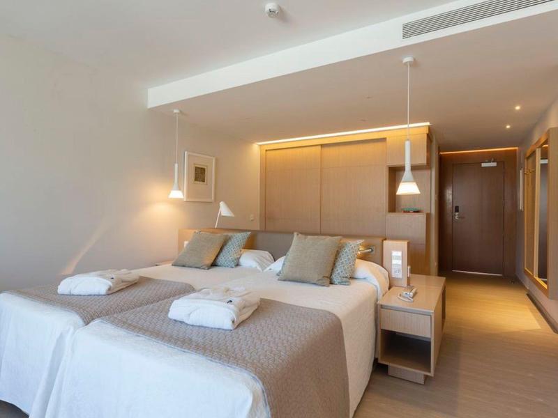 Modernes Hotelzimmer mit Doppelbett, beigen Bettdecken und weichen Kissen, minimalistischem Design.