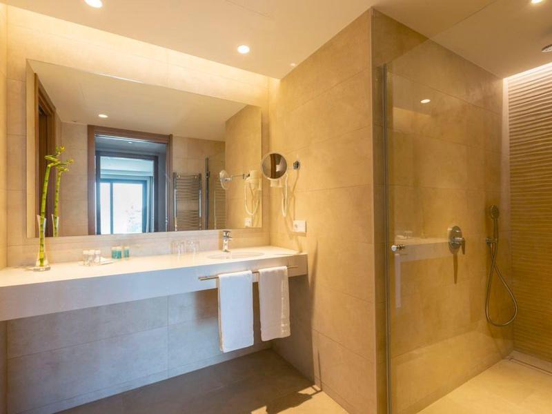 Modernes Hotelbad mit großem Spiegel, Doppelwaschbecken und begehbarer Dusche mit Glaswand.