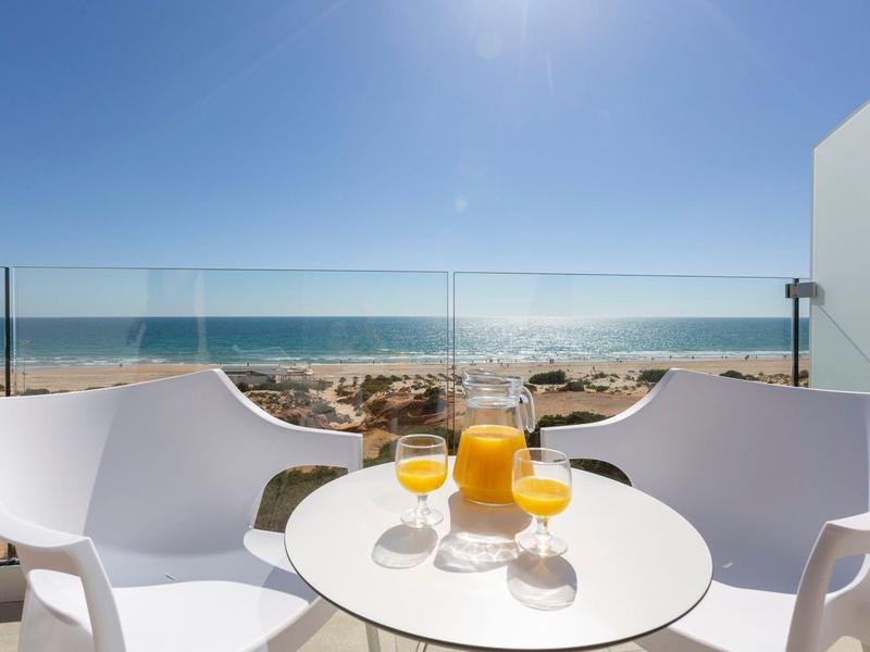 Balkon mit zwei weißen Stühlen und einem Tisch mit Orangensaft, Blick auf den Strand und das Meer.
