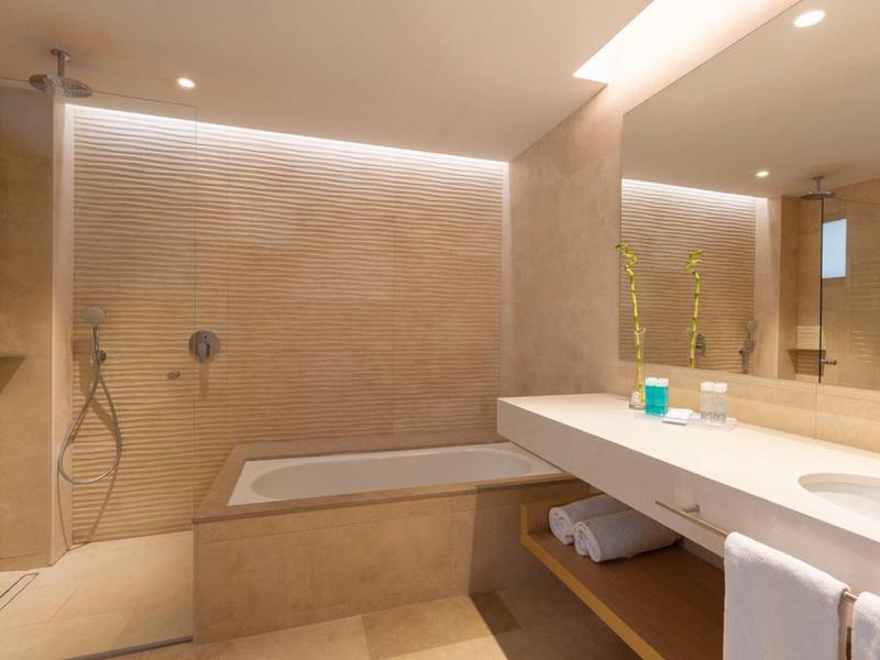 Helles modernes Badezimmer mit Badewanne, großem Spiegel und Waschtisch mit Handtüchern.