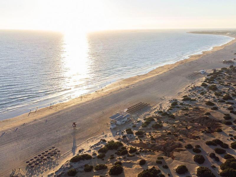 Lange Küste mit Sandstrand und Sonnenlicht, das auf das ruhige Meer scheint.