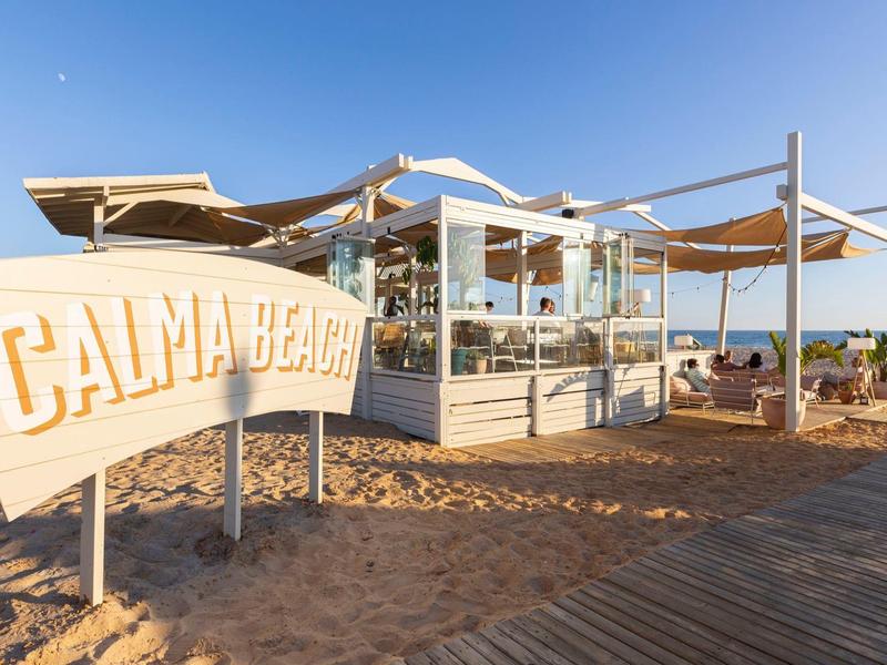Strandrestaurant mit Sonnensegeln und Holzsteg am ruhigen Strand bei Sonnenuntergang