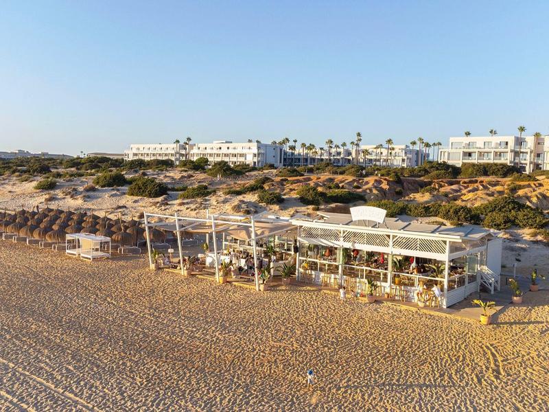 Sandstrand mit Sonnenliegen, Sonnenschirmen und Hotelgebäuden im Hintergrund unter klarem Himmel