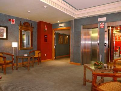 Ein heller, gemütlicher Raum mit Stühlen, Spiegel, Tisch und Aufzug auf grauem Teppichboden.