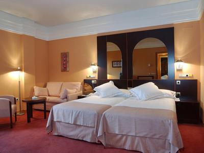 Hotelzimmer mit zwei Einzelbetten, Sofa, Teppichboden und warmen Wandfarben.